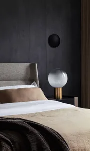 A modern minimalist bedroom with fabric bedding and a glass and metal lamp on a nightstand.