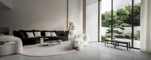 Modern minimalist living room with white marble floor, black sofa, and large windows overlooking greenery.