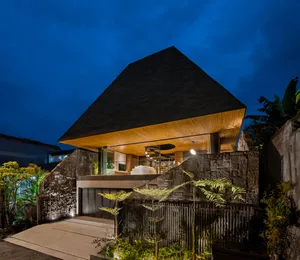 A modern house with a wooden facade and concrete foundation illuminated at night.