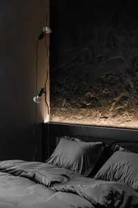 A minimalist bedroom with a bed adorned with dark gray bedding, set against a dark, textured marble wall and illuminated by m