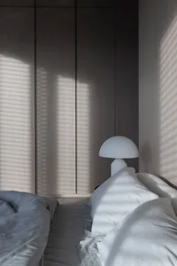 Minimalist bedroom featuring a white bed with soft, fluffy pillows and a white table lamp casting a soft glow.