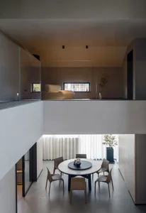 Minimalist living room featuring concrete walls, wood furniture, and a round dining table with chairs.