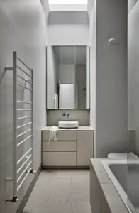 Modern bathroom with white concrete walls, floor, and countertop, a glass partition, and a skylight above a sink.