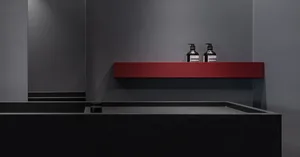 Modern bathroom with minimalist design featuring a concrete sink and a red shelf with dark bottles.
