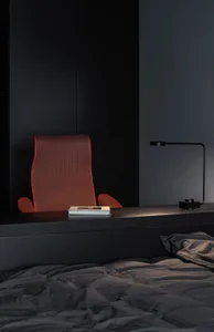 A minimalist bedroom featuring a black bed with gray bedding, a red chair, and a black desk lamp.