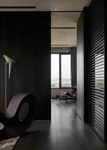 A minimalist residential interior featuring dark wooden floors, a sleek, modern armchair, and a lounge chair with a leather u