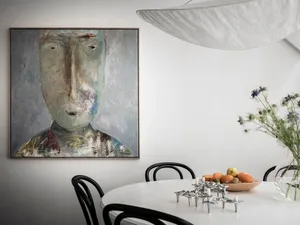 A contemporary dining room featuring a large, abstract portrait artwork on the wall, complemented by a round table, black cha