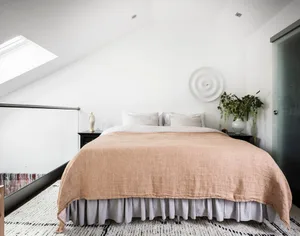 A bedroom featuring a bed with a neutral-toned blanket and matching curtains, set against a white wall with a skylight.