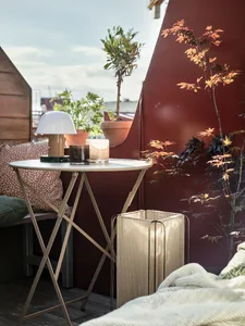 A cozy balcony space featuring a white metal foldable table, metal pots with plants, and a white metal laundry basket.