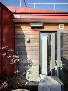 Industrial-style rooftop deck featuring a wooden bench with a green cushion and a metallic heater, under a red roof.