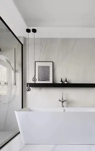 Modern minimalist bathroom featuring a white freestanding bathtub, minimalist pendant lights, and a black floating shelf with