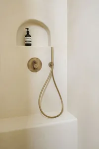A minimalist bathroom shower area with a curved shower head mounted on a white plaster wall.