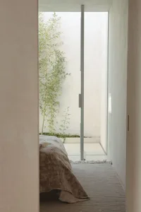 A minimalist bedroom with a bed draped with a neutral-toned textile, surrounded by natural light and greenery.