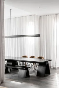 A minimalist dining room with a black table, white curtains, and wooden flooring.