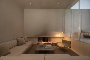 A minimalist living room featuring concrete walls and flooring with a cozy fireplace and comfortable seating.