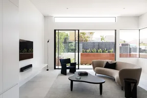 Minimalist living room with a neutral color palette, including a beige sofa, black armchair, and wooden coffee table.