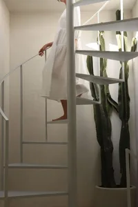 A minimalist metal staircase with a white dress-clad woman descending it.