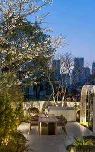 A modern outdoor garden featuring wooden furniture, concrete elements, and lush greenery under a blooming tree.