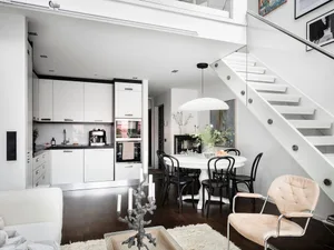 A modern kitchen and dining area featuring white furniture and white walls.