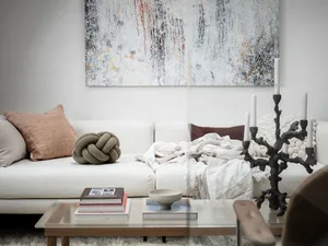 A modern living room with a white sofa, abstract painting, wooden coffee table, and concrete floor.