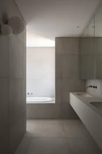 Modern minimalist bathroom with concrete walls and floor, featuring a white bathtub and a white floating vanity with a sink a