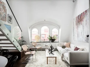 A modern minimalist living room with a white sofa and chairs, arched windows, and abstract paintings.