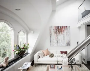 Modern minimalist living room with a white sofa, abstract art, and arched windows overlooking greenery.