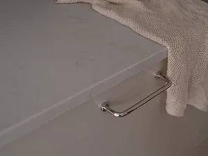 Close-up of a shiny chrome kitchen handle on a marble countertop, with a beige knitted towel draped over the edge.