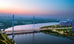 Aerial view of a modern suspension bridge over a wide river during twilight.