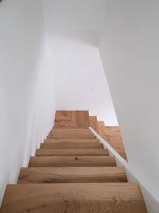 A wooden staircase with white walls and a white handrail leading upwards.
