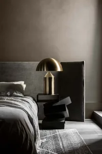 A minimalist bedroom with a metal side table, grey bedding, and a grey headboard.