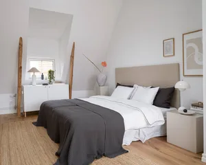 Modern minimalist bedroom with wooden flooring, fabric bedding, and ceramic vase.