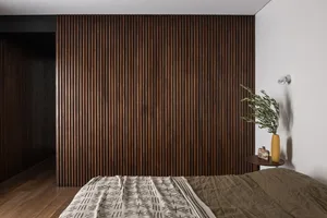A minimalist bedroom with a wooden panel wall and a bed with a patterned blanket and brown sheets.