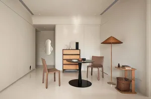 A minimalist dining room featuring a round table with a black base, two chairs with leather seats, and a cabinet with rattan