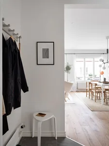 A minimalist entryway featuring a white stool, wall-mounted coat rack, and framed artwork.