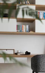 A minimalist home office with a wooden desk, white surfaces, and various books organized on shelves.