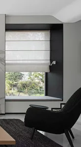 A minimalist living room featuring a window with fabric blinds and a black armchair.