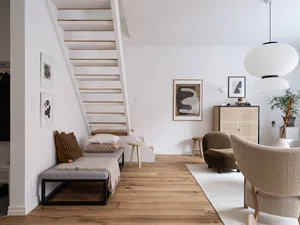 A minimalist living room with wooden floors, a staircase, and modern furniture.