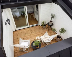 A minimalistic patio with wooden flooring, white furniture, and potted plants.