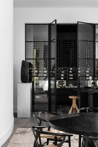 A modern minimalist wine bar with black metal structure and glass doors displaying an extensive collection of wine bottles.