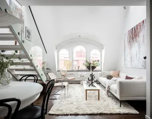 A modern apartment living room with white walls, a white sofa, and a white round dining table.