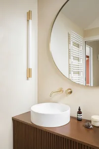 Modern bathroom featuring a ceramic sink and wooden vanity with brass fixtures.