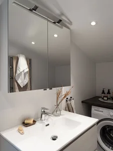 A modern bathroom with a white tile floor and white walls, featuring a white sink, a mirror cabinet, and a washing machine.