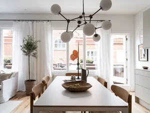 A white dining room with modern design features, white chairs, and a wooden dining table with a bowl of food.