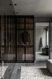 Modern interior design featuring a glass and wood clothes closet with a leather jacket hanging inside.