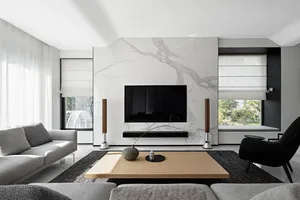 A modern living room featuring a marble accent wall with a flat-screen TV mounted on it, flanked by stereo speakers, and a wo