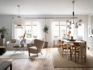 A modern Scandinavian living room with a minimalist design, featuring a white sofa, cushioned armchair, and wooden dining tab