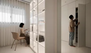 A modern minimalist apartment with a woman sitting on a chair and a man standing in front of a wardrobe.