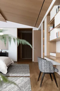 A modern minimalist bedroom with wooden walls, a black and white patterned chair, and a rug with geometric patterns.