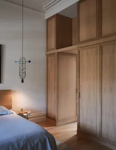 A modern minimalist bedroom featuring wood cabinets and a bed with a simple headboard.